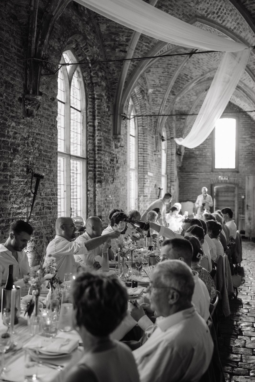Gasten aan tafel onder de gewelven, zwart-wit