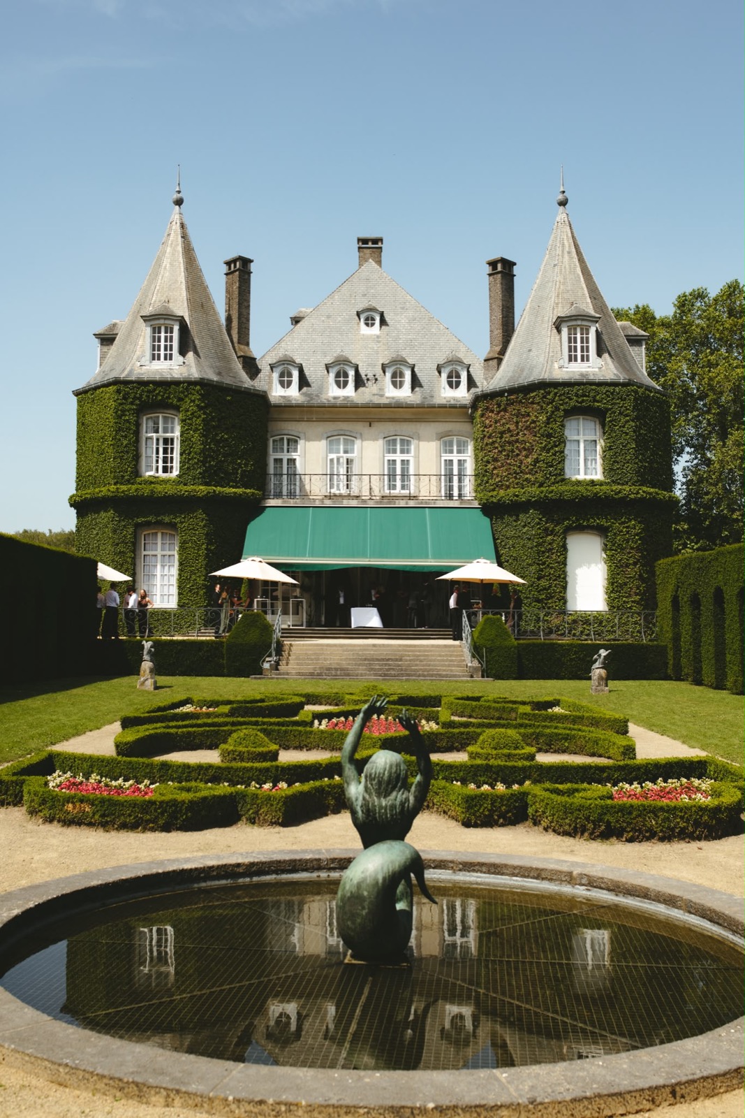 Kasteel met torentjes en klimop, gezien over een fontein met beeld en de formele tuin