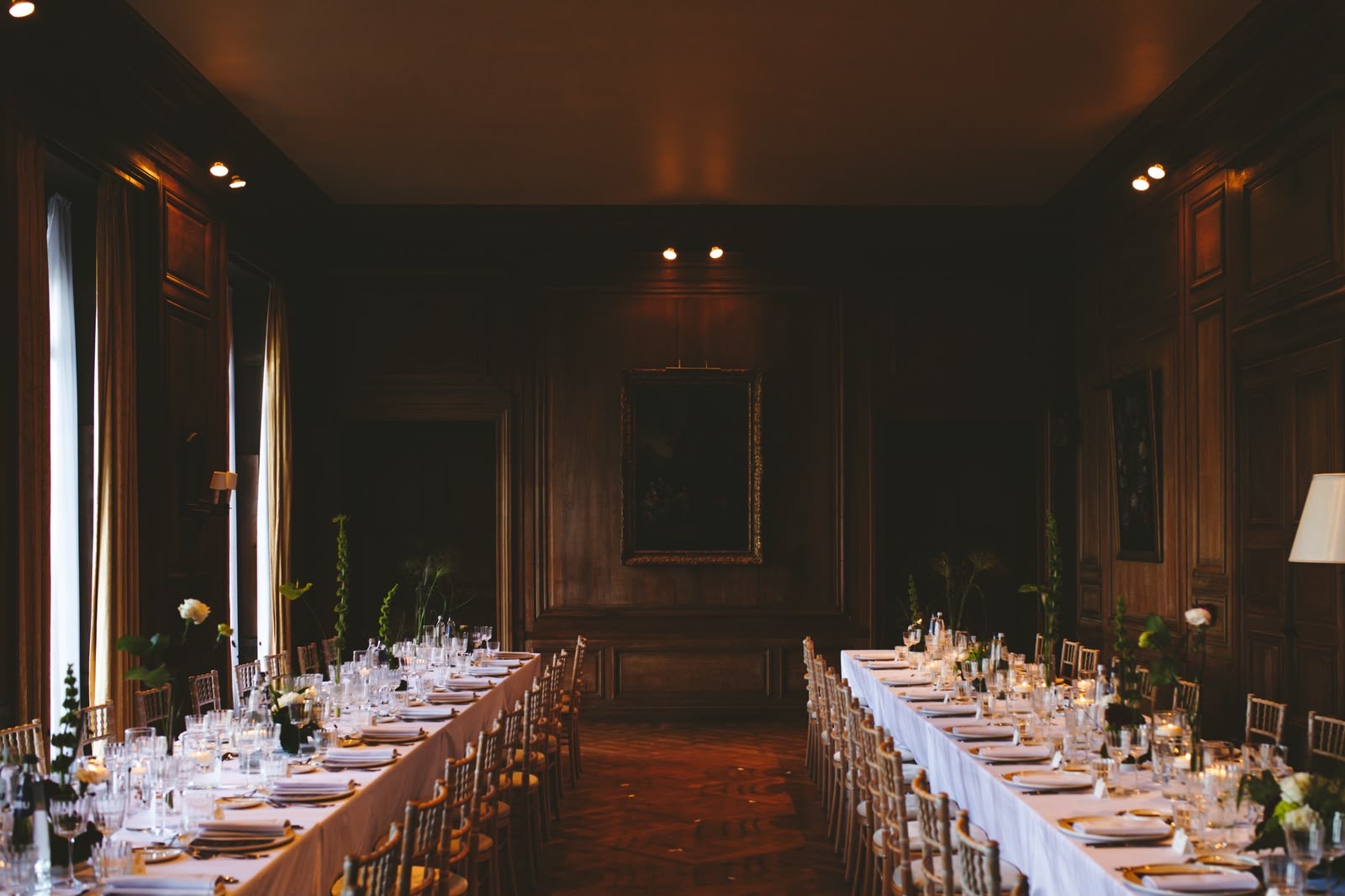 Lange dinertafels in een houten eetzaal met een schilderij aan de wand
